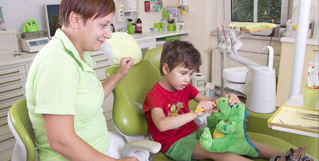 Freundliche Assistentin spielt mit Kind bei der Behandlung beim Zahnarzt